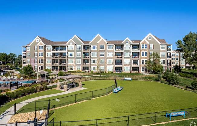 an exterior view of an apartment building with a green field and a tennis court