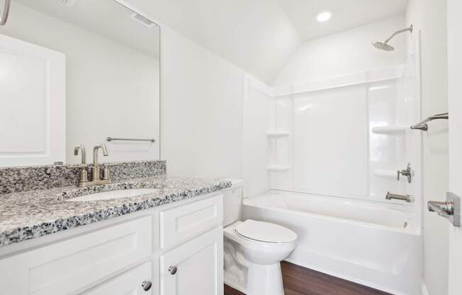 A white bathroom with a granite countertop and a white bathtub.