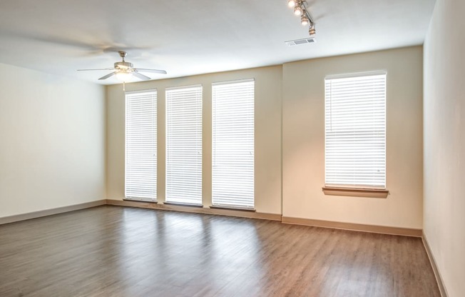 an empty living room with windows and wood floors and a ceiling fan