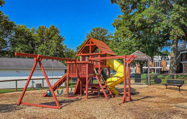 a red swing set with a yellow slide in a park