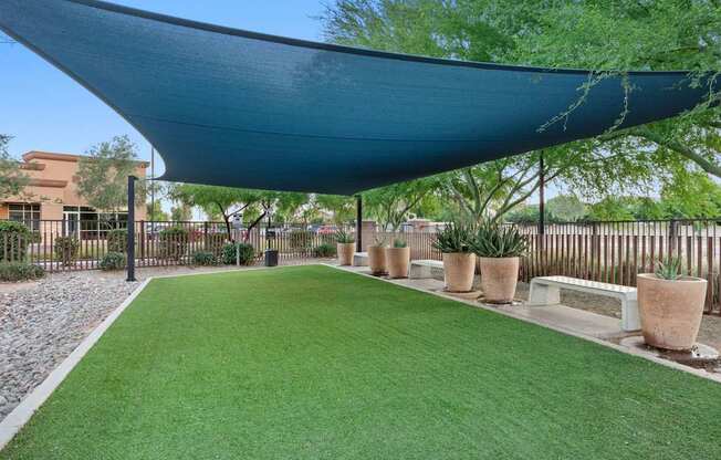A patio with a blue shade sail and artificial grass.