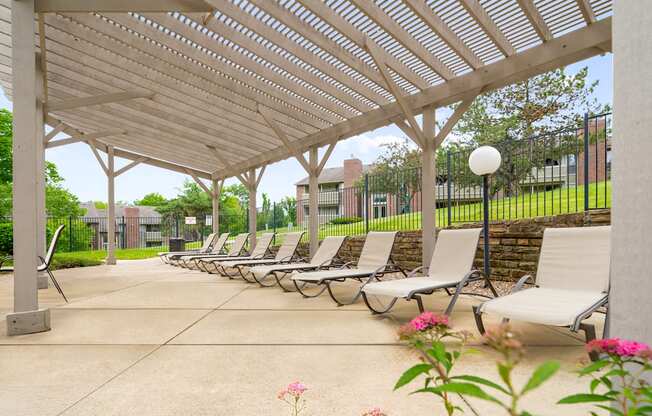 A row of lounge chairs are set up under a white pergola.