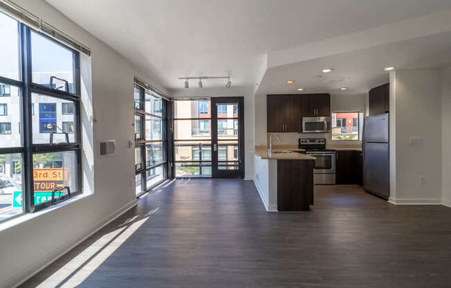 A spacious kitchen and living room with dark wood floors and white walls.