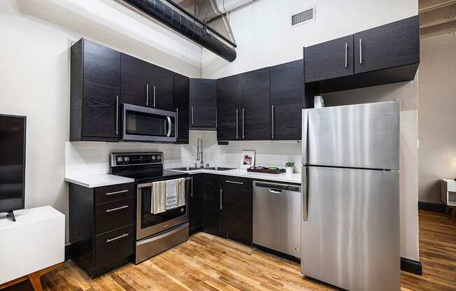 A kitchen with black cabinets and a stainless steel refrigerator - The Kirby