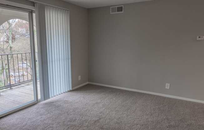an empty living room with a sliding glass door to a balcony