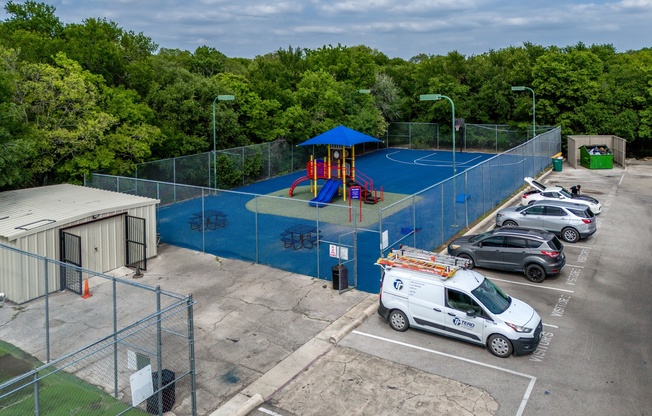 A playground with a blue fence and a white van parked in front of it.