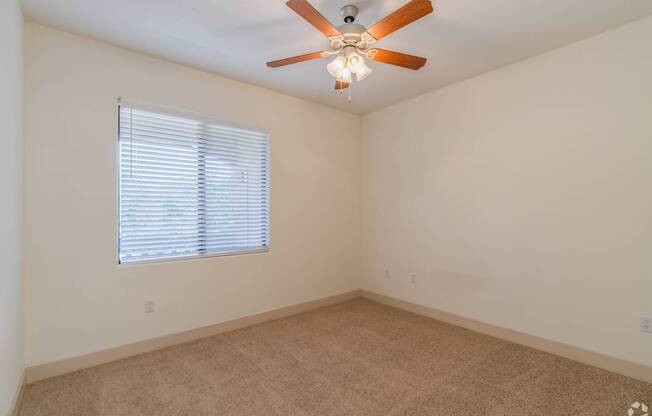 A room with a ceiling fan and a window with blinds.