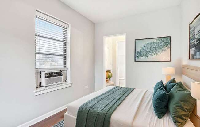 A bedroom with a bed, a window with blinds, a lamp, and a painting on the wall.