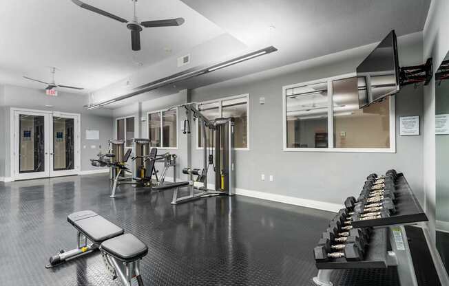 Free weights, strength machines, and mounted TV in fitness center at West 39th Street Apartments.