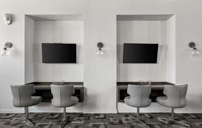 Two chairs are placed in front of two TVs on a wall.
