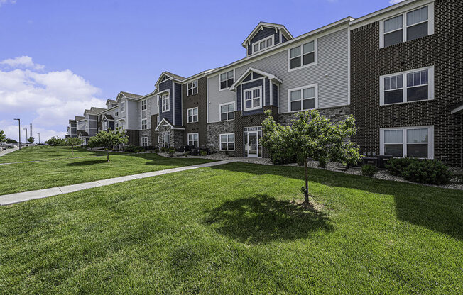 a green lawn with shade trees in front of an apartment building at Trade Winds Apartment Homes in Elkhorn, NE 68022