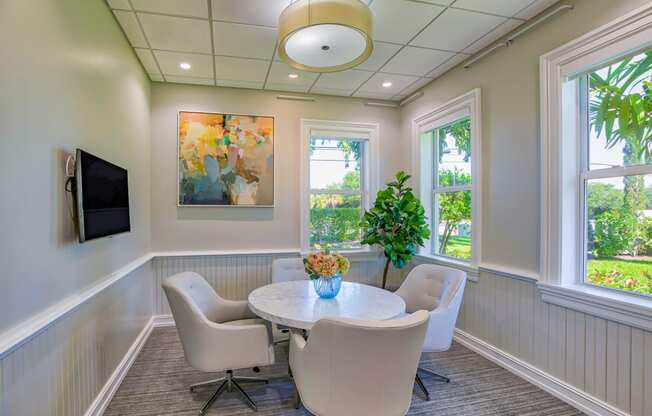 a round table with white chairs and a potted plant in the center of the room