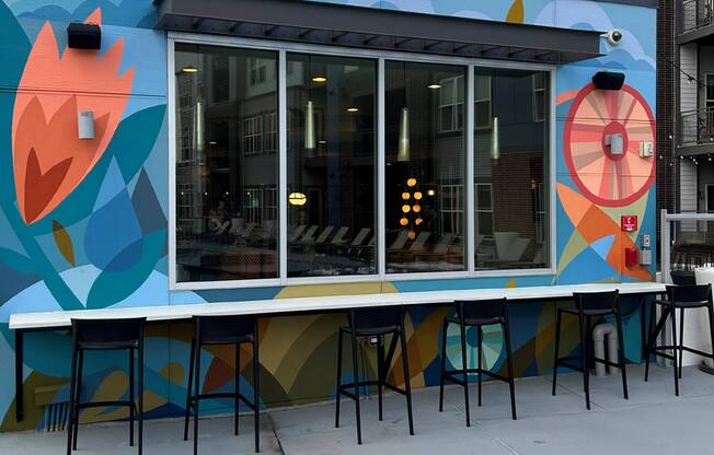 A colorful mural on a wall with a bar stool in front of it.