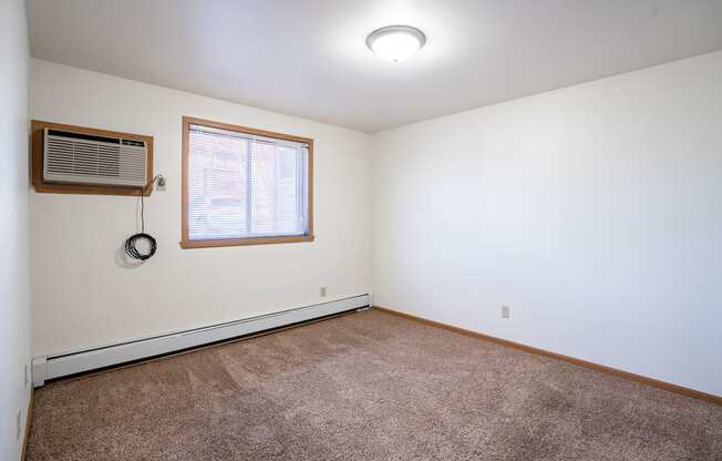 A room with a window and a carpet on the floor. Fargo, ND Birchwood 2 Apartments