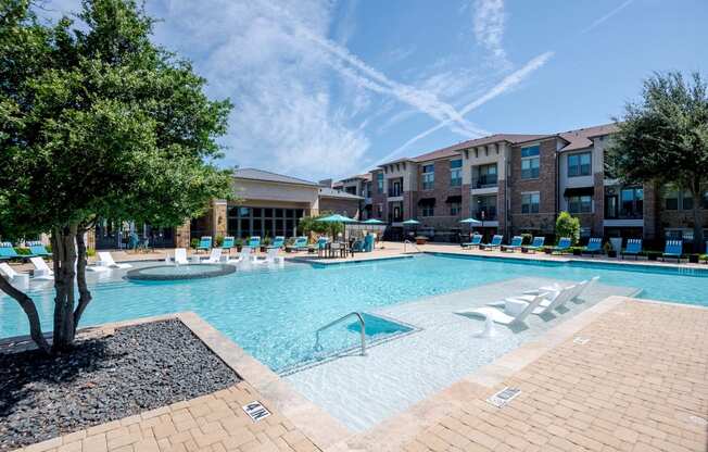 a large swimming pool with lounge chairs in front of an apartment building