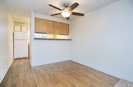 an empty living room with a ceiling fan and a kitchen