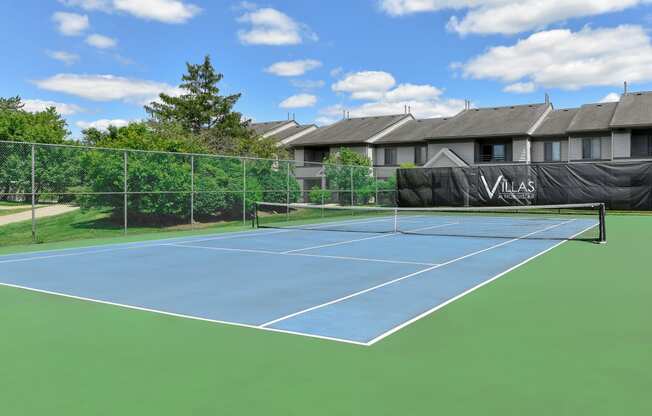 a blue and green tennis court with a house in the background