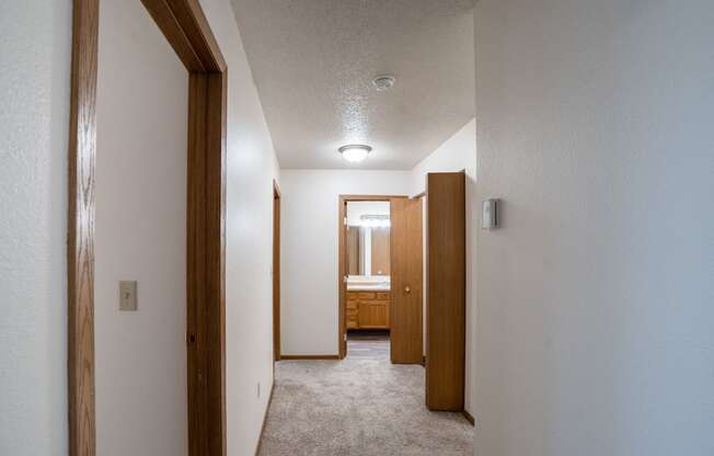 a hallway with a carpeted floor and wooden doors to a bathroom. Fargo, ND  Prairie Park Apartments