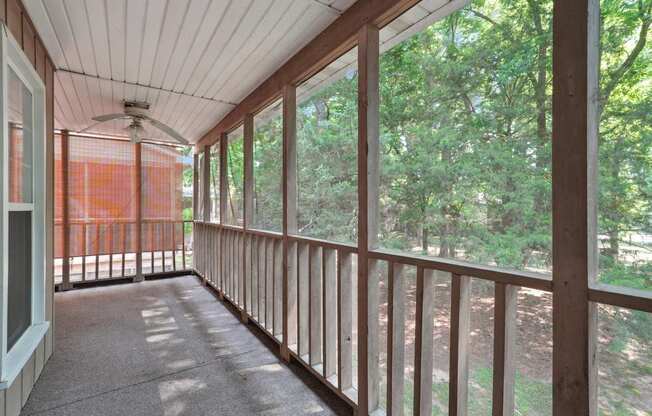 A screened-in balcony with a ceiling fan and a view of trees.