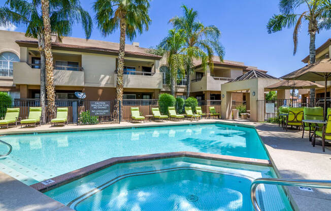 a resort style pool with lounge chairs and umbrellas in front of a building