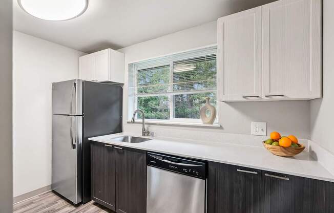 A kitchen with a black fridge and dishwasher, white cabinets, and a window.