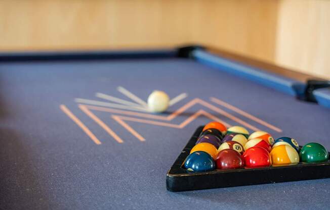 A pool table at the Mastlight with a ball in motion and a rack of balls behind it.