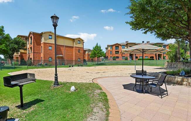 A sunny day at a park with a bench, lamp post and a table with chairs.