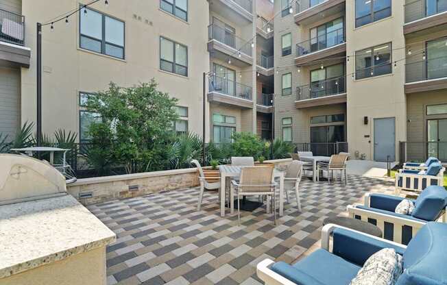 A patio with chairs and tables is surrounded by apartment buildings.