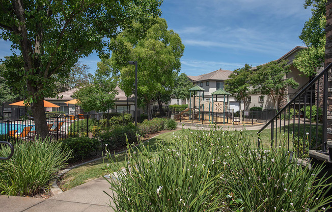 A view of a swimming pool gate and playground with trees at Stoneridge Apartments, California, 95661