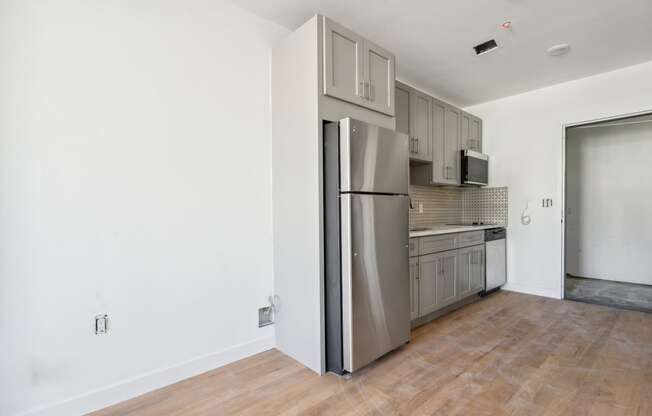 an empty living room with a refrigerator and a kitchen