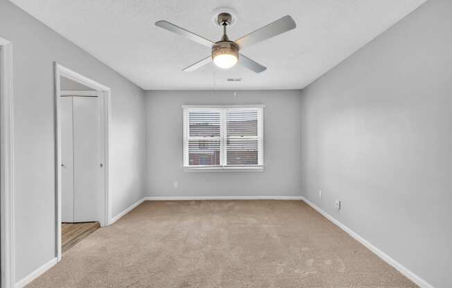 an empty bedroom with a window and ceiling fan