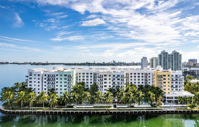 a large building with palm trees in front of a body of water