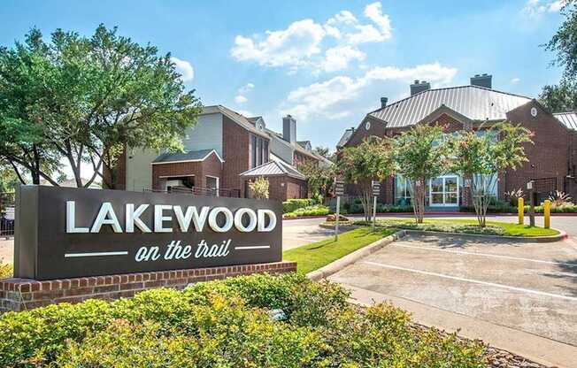 A community entrance sign here at Lakewood on the Trail with landscaped greenery, brick buildings, and a welcoming front drive, creating a polished and inviting first impression.