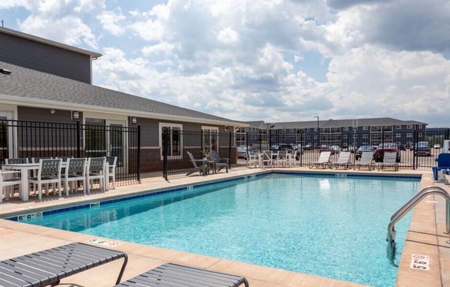 a swimming pool with lounge chairs and tables and a building in the background