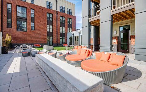 a patio with orange and gray chairs and a brick building