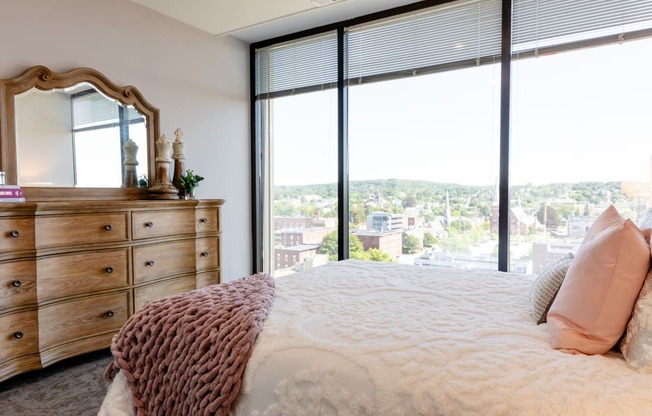 a bedroom with a large window and a dresser with a mirror