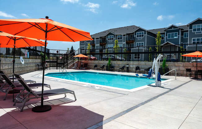 A pool surrounded by chairs and umbrellas with apartment buildings in the background.