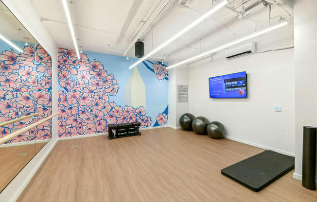 a yoga studio with a wooden floor and a wall with a screen and exercise balls  at Link Apartments® H Street, Washington, 20002