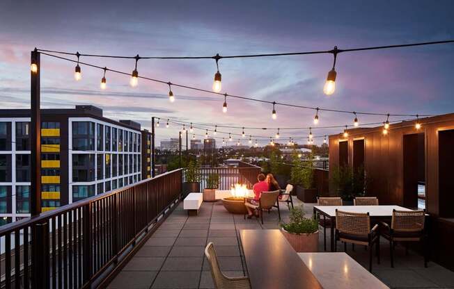 A rooftop patio with people sitting and string lights hanging above.