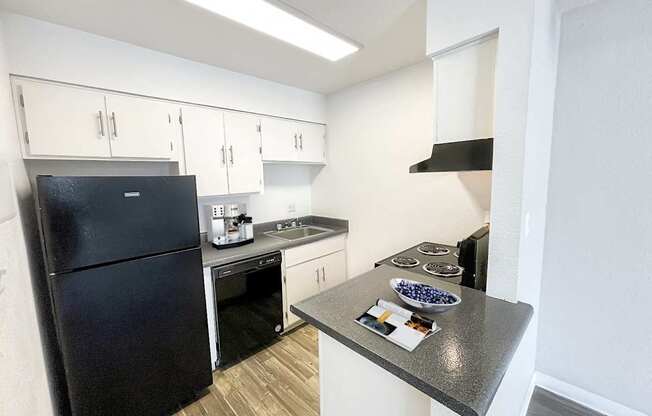 A black refrigerator is in a kitchen with white walls.