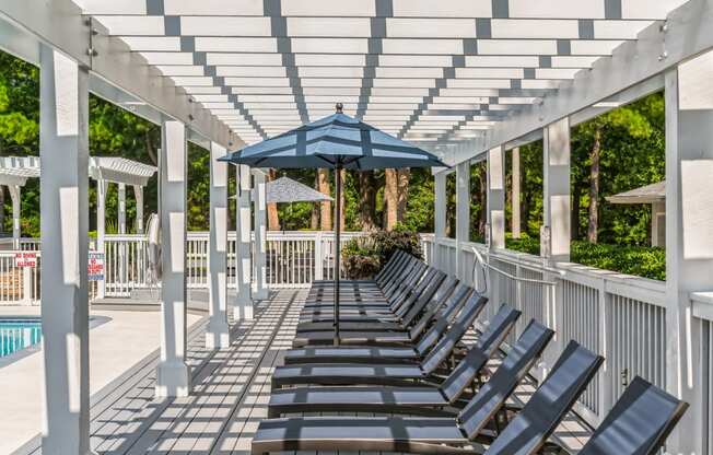 a row of lounge chairs under a white covered pavilion with an umbrella