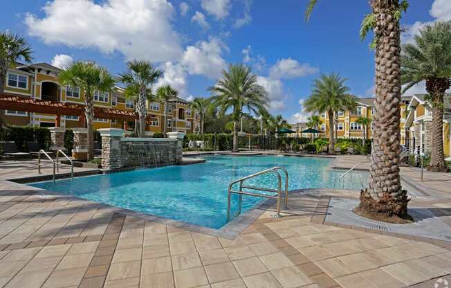 A pool surrounded by palm trees and a building in the background.