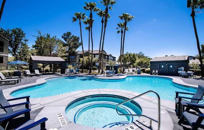 Large swimming pool and spa surrounded by Palm Trees and chairs.