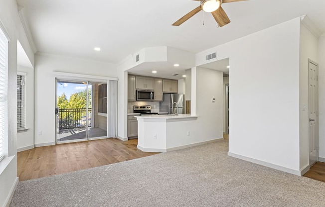 an empty living room with a kitchen and a ceiling fan