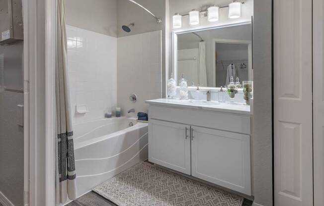A white bathroom with a tub, sink, and mirror.