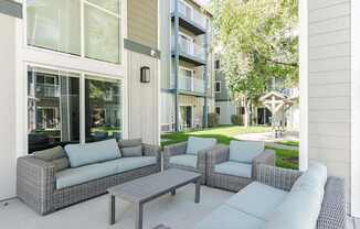 A patio with a grey sofa, two chairs and a table.