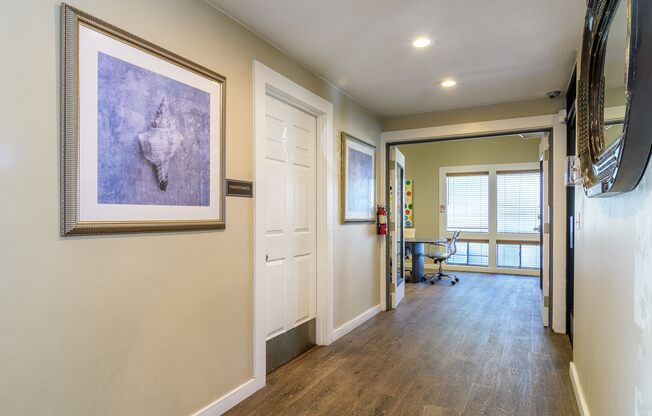A hallway with a painting on the wall and a mirror on the right side.