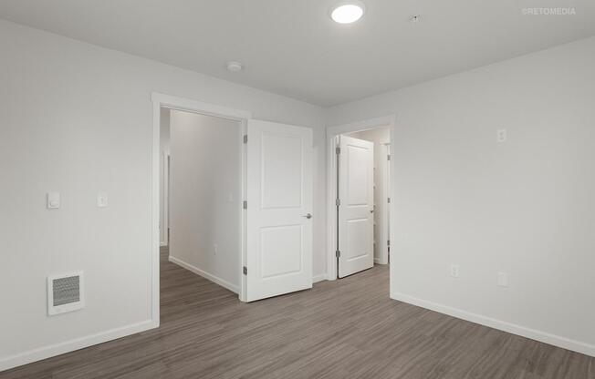 A room with white walls and wooden flooring with two doors.