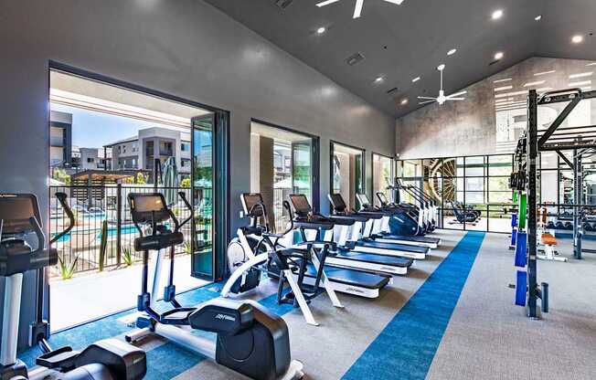 a gym with cardio equipment and windows with a view of a building