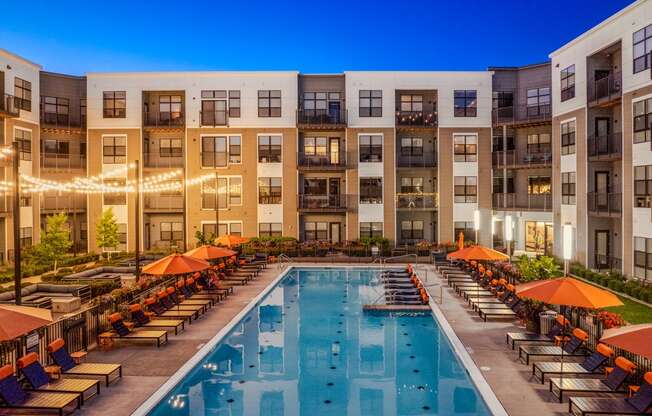 an outdoor pool with lounge chairs and umbrellas in front of an apartment building